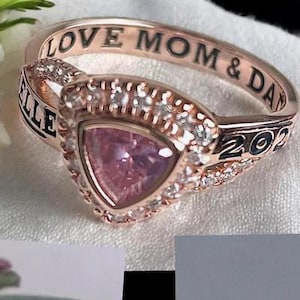 May include: Rose gold ring with a pink stone and a band that says "LOVE MOM & DAD 2029" and "ERIELLLE".
