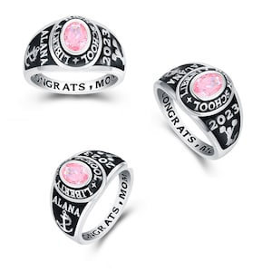 May include: A silver class ring with a black enamel band. The ring features a pink stone, the words "Liberty School" and "2023", and an anchor. The band is inscribed with "Alana" and "Congrats, Mom".
