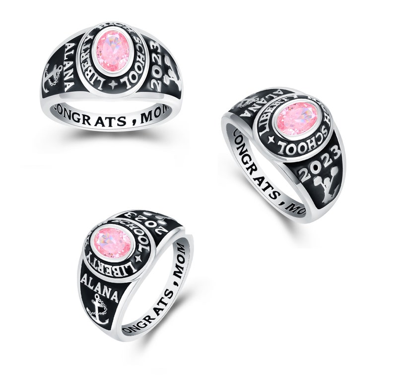 May include: A silver class ring with a black enamel band. The ring features a pink stone, the words "Liberty School" and "2023", and an anchor. The band is inscribed with "Alana" and "Congrats, Mom".