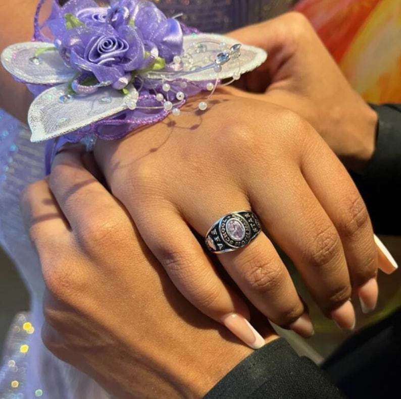 May include: A close-up of a hand wearing a silver class ring with a purple stone. The ring has the words "SCHOOL" and "FFA" engraved on it.