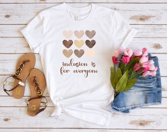 May include: White t-shirt with a graphic of brown hearts and the text "inclusion is for everyone".