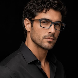 May include: Eyeglasses featuring rectangular black frames with a matte finish and distinct wooden temples. The glasses have a classic bridge design and are worn by a person with dark curly hair, who is dressed in a solid black button-down shirt.