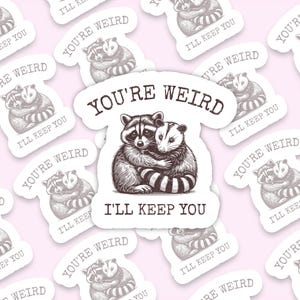 May include: A white sticker with black text and a black and white illustration of a raccoon and opossum hugging. The text reads "You're Weird I'll Keep You."