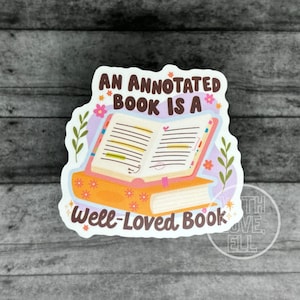 May include: A sticker with an illustrated open book with handwritten notes and highlights. The text reads "An annotated book is a well-loved book".