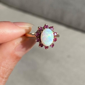 May include: A gold ring with a white opal gemstone surrounded by a halo of pink rubies.