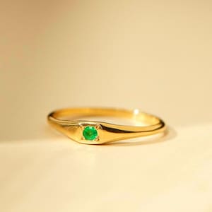 Puede incluir: Un anillo de oro con una sola esmeralda verde engastada en el centro.