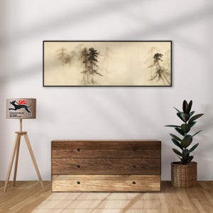 K&ouml;nnte beinhalten: Gerahmtes Landschaftsgem&auml;lde mit schwarzem Rahmen. Das Kunstwerk zeigt eine neblige Waldszene in Braun- und Schwarzt&ouml;nen. Eine Holzkommode mit drei Schubladen und eine Stehlampe mit Logo befinden sich im Vordergrund.