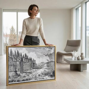 May include: A rectangular framed wall art piece featuring a black and white historical etching of a cityscape with classical architecture, ruins, and figures. The artwork is enclosed in a thin gold-colored frame and displays detailed line work.