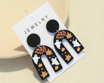 May include: A pair of black Halloween-themed earrings with a ghost, pumpkin, and leaf design. The earrings are shaped like an arch and have a black circle at the top.