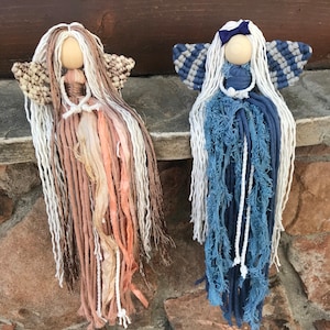 May include: Two handmade yarn dolls with long white hair and wings. The doll on the left has a peach and brown dress and the doll on the right has a blue dress.