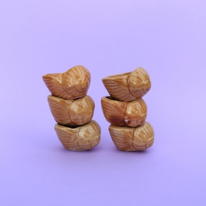 Peut inclure: Deux piles de quatre petites tasses en céramique brunes avec une surface texturée. Les tasses sont empilées les unes sur les autres, la tasse du haut de chaque pile étant face au spectateur.
