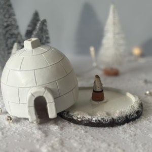 以下が含まれることがあります： 白いセラミック製のイグルー型の香炉に、茶色と白の香りのコーンが置かれています。ベースは白と茶色のセラミック製で、雪の表面のようにデザインされています。