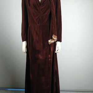 May include: A long brown velvet dress with a gold sequined trim around the neckline and hem. The dress has a V-neckline and a sash that ties around the neck.