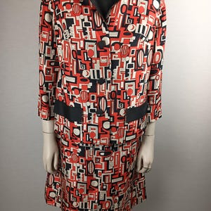 May include: A red, black, and white geometric print skirt suit. The jacket has a black collar and a button closure. The skirt is knee-length.