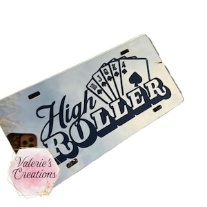 May include: A silver license plate with a black design that says "High Roller" with playing cards in the background.