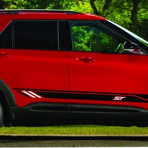 Könnte beinhalten: Ein roter Ford Explorer ST mit schwarzen Seitenstreifen und schwarzen Rädern. Das Auto steht auf einer grasbewachsenen Fläche.