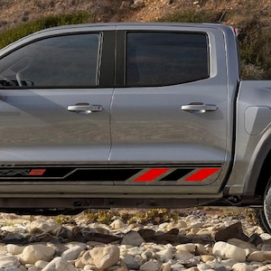 May include: A grey pickup truck with black detailing and red stripes. The truck has black wheel arches and silver alloy wheels. The side of the truck features the text "ZR2" in black and red.