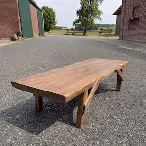 May include: A rectangular low-profile coffee table constructed from dark brown stained wood. The table features a thick, solid tabletop surface supported by four sturdy vertical legs, each reinforced with angled wooden support braces.