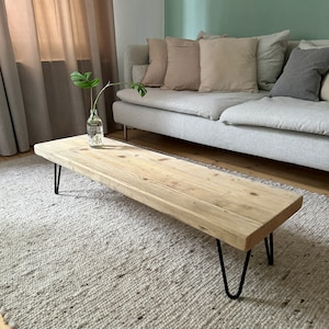 Könnte beinhalten: Ein rustikaler Holz-Couchtisch mit schwarzen Haarnadelbeinen. Der Tisch steht auf einem cremefarbenen Teppich in einem Wohnzimmer.