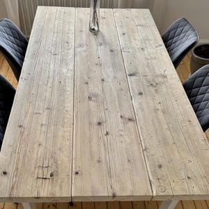 Könnte beinhalten: Ein rechteckiger Esstisch aus hellem, verwittertem Holz mit sichtbarer Maserung, Ästen und natürlichen Unregelmäßigkeiten. Der Tisch ist von vier dunkelgrauen Stühlen mit gestepptem Rautenmuster im Polsterbezug umgeben.