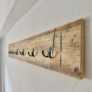 Peut inclure: Un porte-manteau mural rectangulaire fabriqué à partir d'une seule pièce de bois récupéré brun clair avec un grain visible et des nœuds naturels. Le support comporte six crochets en métal noir régulièrement espacés sur la face avant.