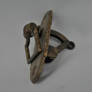 Puede incluir: Aldaba de puerta antigua de latón con un mango redondeado y una placa trasera decorativa. La aldaba tiene un aspecto envejecido, con signos visibles de edad y uso. El diseño presenta un mango en forma de anillo y un brazo curvado.