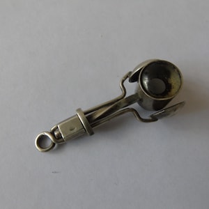 May include: A silver-toned metal ice cream scoop with a mechanical spring-loaded release mechanism. The tool features a circular bowl, a handle with a small loop at the end for hanging, and a lever system designed to eject scoops of food.