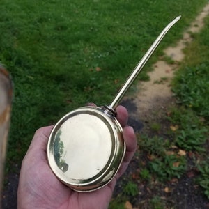 Op de afbeelding: Een oliefles van messing met een lange tuit. De fles is rond en heeft een glanzende afwerking.