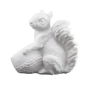Könnte beinhalten: Weiße Keramik-Eichhörnchenfigur, die eine weiße Eichel hält. Das Eichhörnchen hat einen buschigen Schwanz und sitzt auf seinen Hinterbeinen.