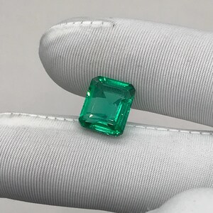 Könnte beinhalten: Ein leuchtend grüner Edelstein im Smaragdschliff. Der Edelstein hat eine lebendige grüne Farbe und scheint facettiert zu sein, mit einer quadratischen Form. Der Edelstein wird vor einem weißen Hintergrund präsentiert.