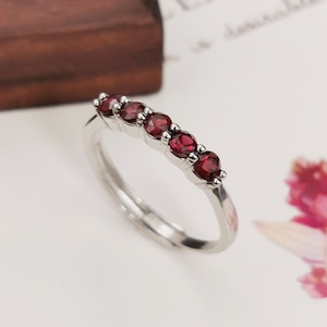 May include: A silver band ring with six red gemstones set in a row. The ring is on a white background.