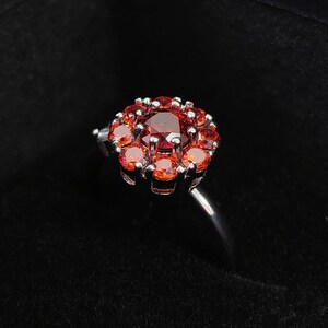 Op de afbeelding: Een zilveren ring met een cluster van rode edelstenen in de vorm van een bloem.