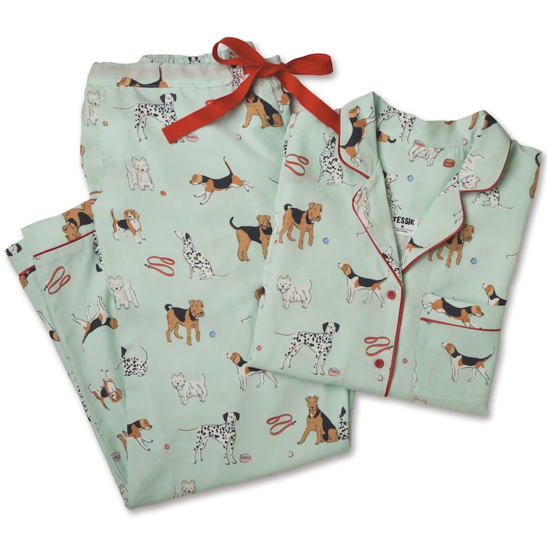 Pode incluir: Um conjunto de pijama verde menta com acabamento vermelho e um padr&atilde;o de v&aacute;rias ra&ccedil;as de c&atilde;es. A parte superior tem fecho de bot&otilde;es e uma gola com a palavra "Tessie" impressa.
