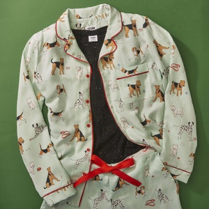 Pode incluir: Um conjunto de pijama azul claro e branco com estampa de cachorro. A parte superior tem um fecho de bot&atilde;o na frente e mangas compridas. As cal&ccedil;as t&ecirc;m uma cintura el&aacute;stica. O conjunto apresenta uma variedade de ra&ccedil;as de c&atilde;es em diferentes poses.