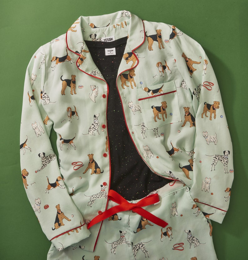 Pode incluir: Um conjunto de pijama azul claro e branco com estampa de cachorro. A parte superior tem um fecho de bot&atilde;o na frente e mangas compridas. As cal&ccedil;as t&ecirc;m uma cintura el&aacute;stica. O conjunto apresenta uma variedade de ra&ccedil;as de c&atilde;es em diferentes poses.
