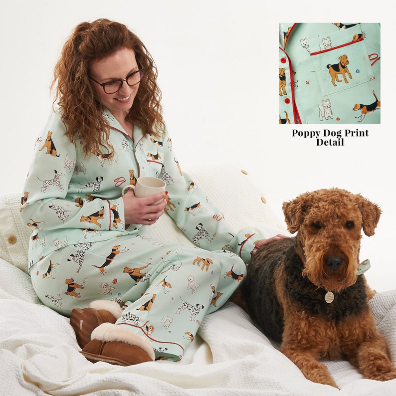 Pode incluir: Uma mulher vestindo um pijama verde claro com estampa de cachorro. O pijama tem uma borda vermelha e uma parte superior com bot&otilde;es. A mulher est&aacute; sentada em uma cama branca com um cachorro marrom ao lado dela. O cachorro est&aacute; usando uma coleira marrom com uma etiqueta. A imagem inclui o texto "Poppy Dog Print Detail".
