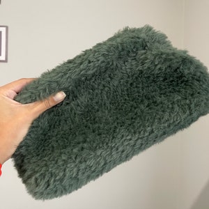 May include: A soft, plush green clutch bag made of faux fur.