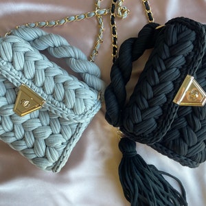 May include: Two crocheted handbags with gold chain straps and tassels. One bag is light blue and the other is black.