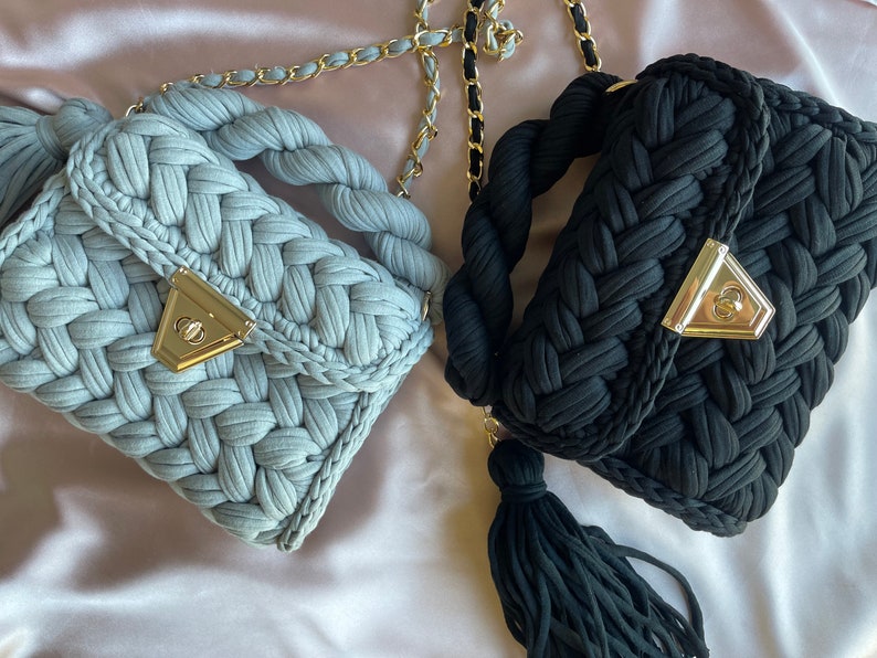 May include: Two crocheted handbags with gold chain straps and tassels. One bag is light blue and the other is black.
