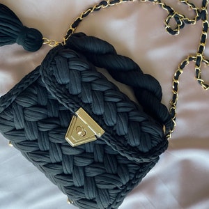 May include: A black woven handbag with a gold chain strap and a tassel. The bag has a gold clasp.