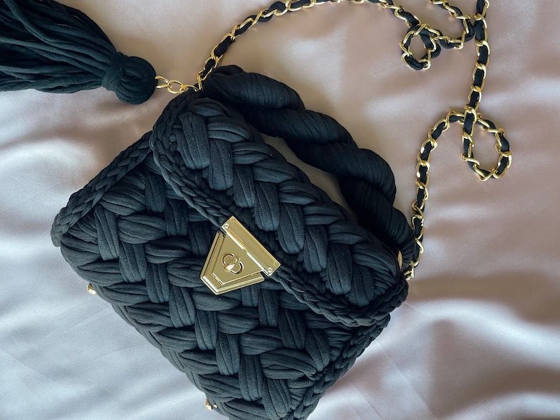 May include: A black woven handbag with a gold chain strap and a tassel. The bag has a gold clasp.