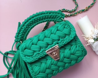 May include: A small green crocheted handbag with a gold chain strap and a gold clasp. The bag has a tassel on the bottom.