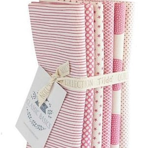 Może przedstawiać: Zestaw sześciu różowych i białych kwadratów z tkaniny z różnymi wzorami, w tym paski, kropki i gwiazdki. Tkanina jest związana wstążką z napisem "Tilda Collection Classic Basics".