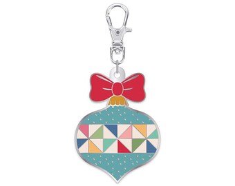May include: A Christmas ornament-shaped keychain with a red bow and silver clasp. The ornament is teal with a geometric pattern of colorful triangles. A festive accessory for keys or bags.