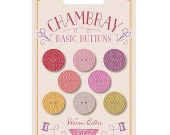 May include: A set of eight warm-toned, fabric-covered buttons with a Chambray Basic Buttons label. The buttons are in shades of pink, red, and yellow. The label also says "Warm Colors" and features the Tilda logo.