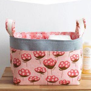 May include: A divided basket with a floral pattern in pink and brown. The basket has a gray rim and handles, and the text "DIVIDED BASKET" is at the top. The basket is on a wooden surface.