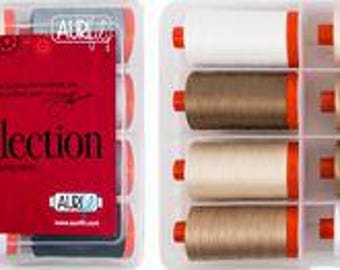 Könnte beinhalten: Ein Set mit 12 Spulen Aurifil-Garn in einem durchsichtigen Kunststoffkoffer. Die Spulen sind in zwei Reihen mit jeweils sechs Spulen angeordnet. Die Spulen sind mit "The Basics Collection" beschriftet und zeigen eine Vielzahl von Farben, darunter Weiß, Beige, Grau und Schwarz.