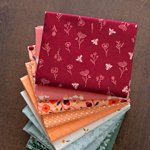 May include: A stack of folded fabric squares in a gradient of colours ranging from deep burgundy to light pink, orange, white, and various shades of green. Each piece of fabric features distinct patterns including floral motifs, bees, and geometric lines.