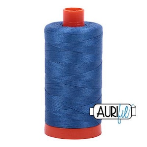 Op de afbeelding: Een spoel blauw garen met een rode boven- en onderkant. De draad is strak opgerold en de spoel heeft het Aurifil-logo aan de zijkant. Deze draad wordt waarschijnlijk gebruikt voor naai- of quiltprojecten.
