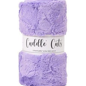 May include: A roll of lavender Cuddle Cuts minky fabric. The fabric is soft and plush, with a subtle pattern. The label reads "Cuddle Cuts 2 Yard Cuddle" minky fabric precut.